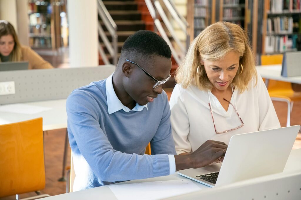 Two diverse students studying together on a laptop in a bright library setting.